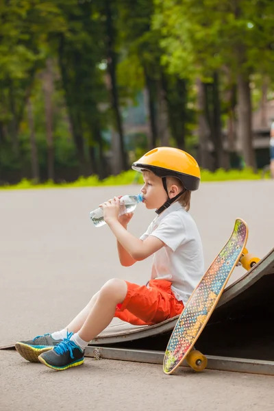 ボードや飲み物、ワットの横にあるヘルメットに座っている少年 — ストック写真