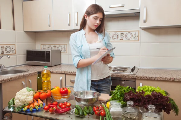 Chica joven escribe receta de ensalada de dieta en la cocina  . — Foto de Stock