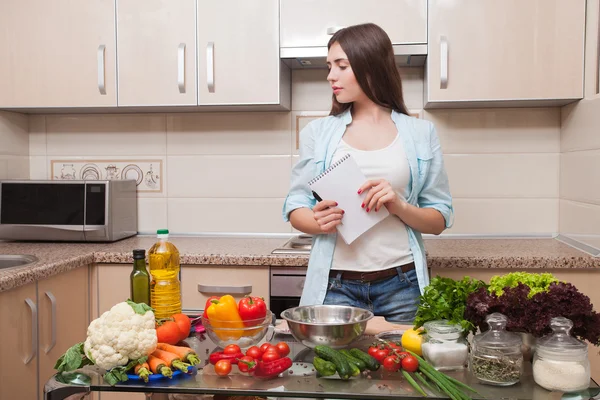 Una chica escribe una receta de ensalada en un cuaderno. Ella está en casa en h — Foto de Stock