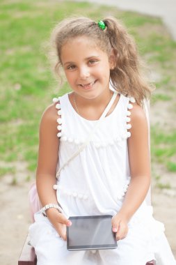 Kız bir bankta oturan ve gülümseyen . Tableti kullanıyor. .