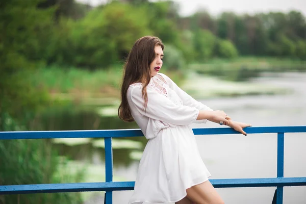 Bella ragazza in un abito bianco in piedi nel parco sul ponte . — Foto Stock