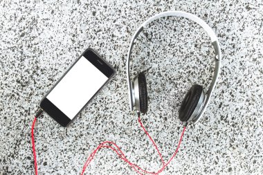 Boş beyaz ekranlı akıllı telefon, gri mermer arka planda kulaklıklarla yakında yatıyor . 