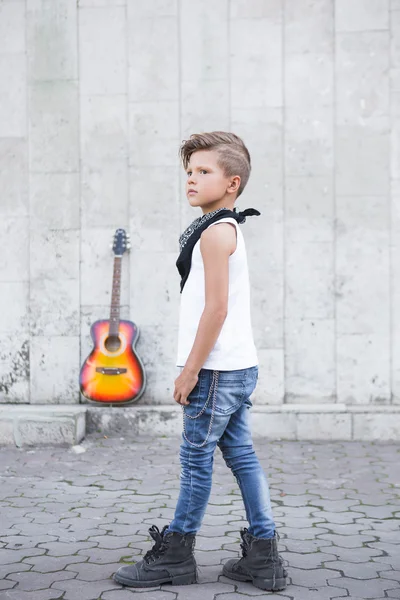 Malý chlapec stojí na pozadí kytaru. On stojí bokem — Stock fotografie