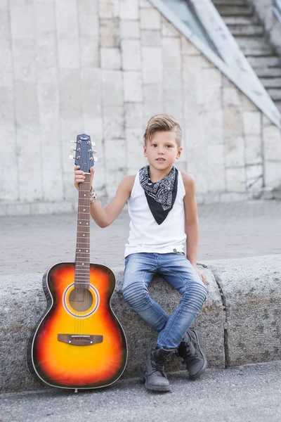 앉아서 한 손으로 기타를 들고 세련 된 작은 소년 — 스톡 사진