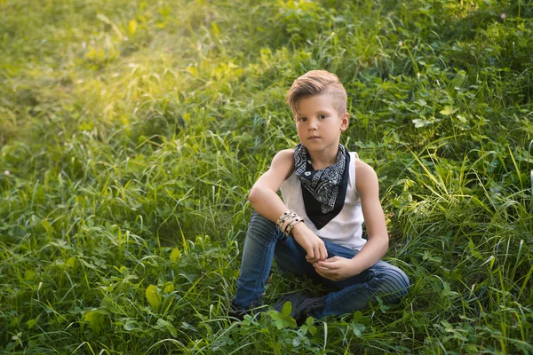 Stylový chlapec sedící na trávě. Je velmi mladý . — Stock fotografie