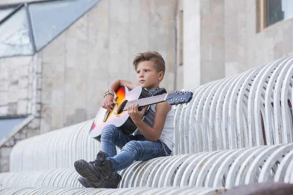 Stylish little boy learns to play the guitar . He was good at it