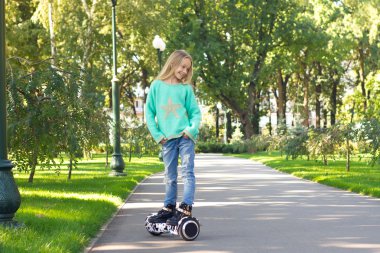 Elektrikli scooter kullanan küçük bir kız ellerini cebine katlayıp başka bir yere bakıyor. .