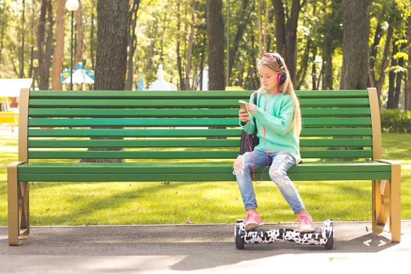 La ragazza con le cuffie seduta sulla panchina. Ha uno zaino. — Foto Stock
