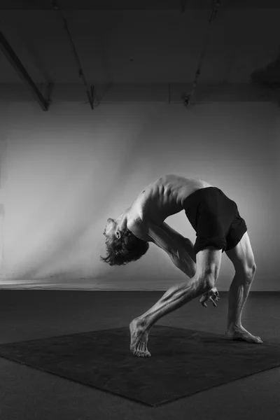 Young stong man dancing in the studio. Flexible body.Black and white.Full length. Side view.Fit sporty man doing backbend exercise