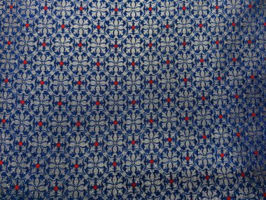 Zengin mavi ve gümüş ipliklerle dokunmuş karmaşık bir geometrik çiçekli kumaş, zamansız zarafet ve zarif işçilik sergiliyor..