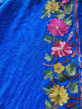 El yapımı Kaşmir çiçekli kenar, dokulu mavi kumaşı zarif işçilikle zenginleştirir..