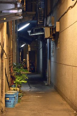 Tayvan - 19 Ekim 2025 Xindian Bölgesi, New Taipei City 'deki binalar arasında dar bir ara sokak, saksı bitkileri, mavi kovalar, elektrik kabloları, drenaj boruları ve park halindeki araç..