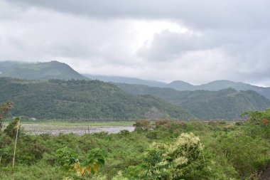 Lanyang Nehri vadiden kıvrılarak geçiyor yemyeşil bitki örtüsü, kum yığınları ve sık ormanlarla kaplı dağlarla bulutlu gökyüzü altında tarihi Pobuwo seti, Sanxing, Yilan.