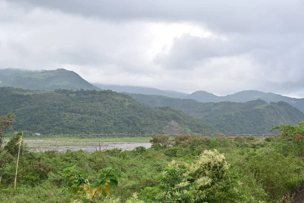 Lanyang Nehri vadiden kıvrılarak geçiyor yemyeşil bitki örtüsü, kum yığınları ve sık ormanlarla kaplı dağlarla bulutlu gökyüzü altında tarihi Pobuwo seti, Sanxing, Yilan.