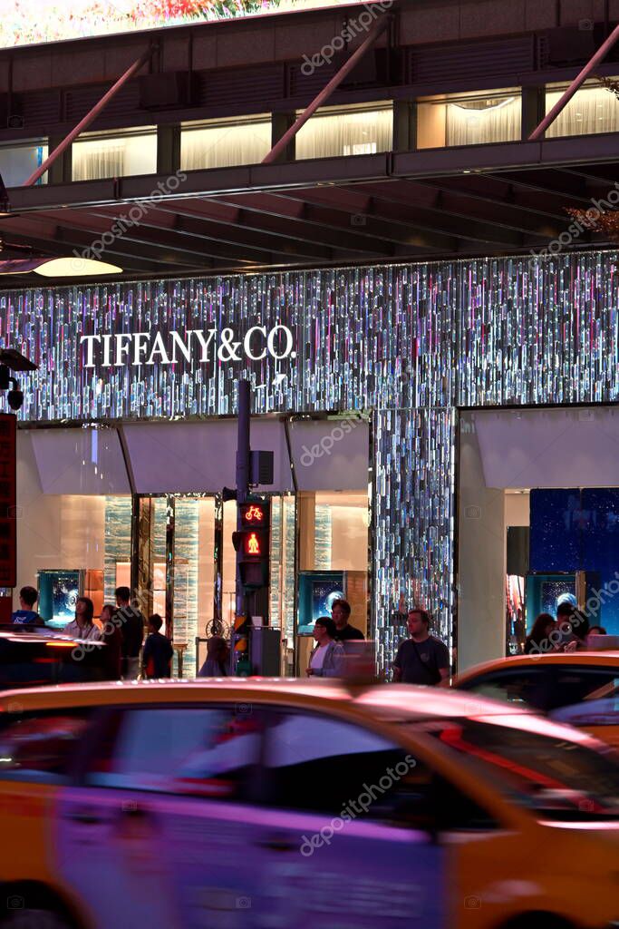 Taiwan - Oct. 26, 2025: Illuminated Tiffany & Co. storefront with distinctive architectural facade and blurred yellow taxis passing in evening traffic, New York City street scene.