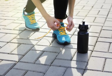 Genç kadın üzerinde bir döşeme üzerinde spor ayakkabı ayakkabı bağcığı bağlama. Bir şişe su yanında duruyor. Açık havada egzersiz