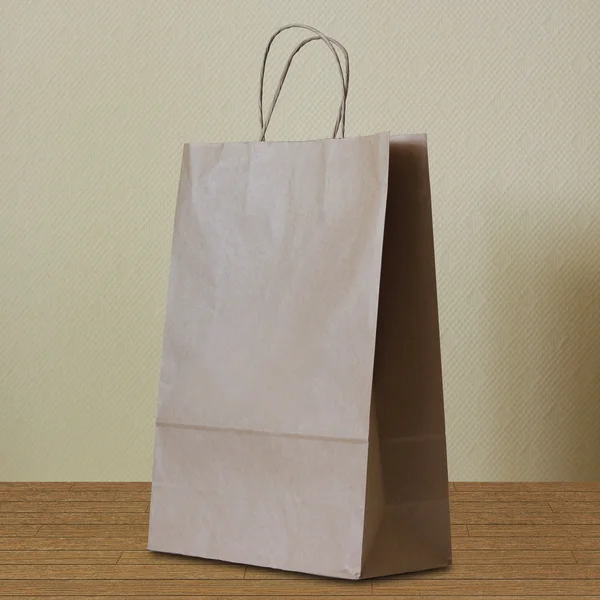 Brown paper bag with handles stands on a wooden floor. — Stock Photo, Image
