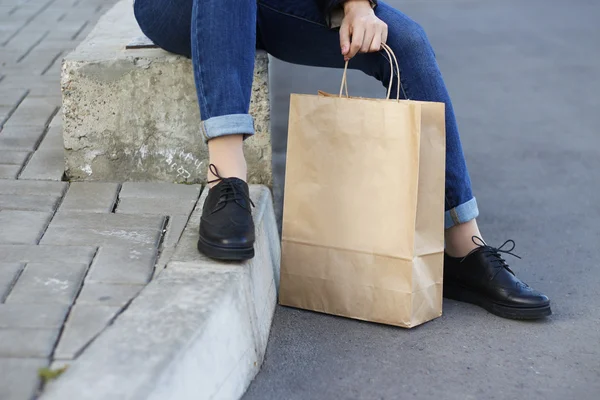 Mädchen in schönen Schuhen sitzt neben einer Papiertüte. — Stockfoto