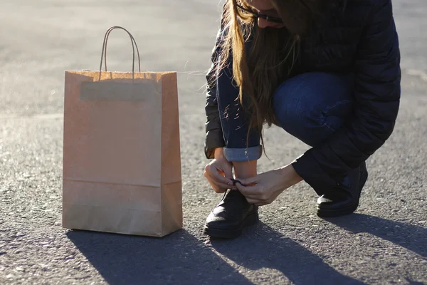 Meisje banden de veters op de mooie schoenen. Daarna is een papieren zak. — Stockfoto