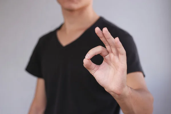 Hombre joven en camiseta negra muestra signo OK. Aislado en la espalda gris —  Fotos de Stock