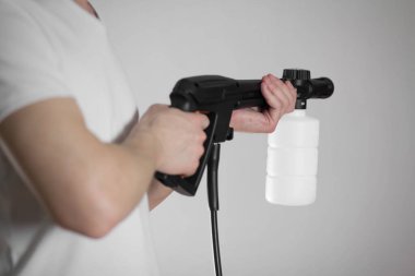 Adamın elinde yüksek basınçlı çamaşır makinesi var. Yakın plan. Gri bir arkaplanda izole edilmiş.