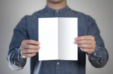 Bir adam beyaz bir kağıt parçası tutuyor. Bir adamın elinde bir el ilanı. Mesajın için hazır. Gri bir arkaplanda izole edilmiş.