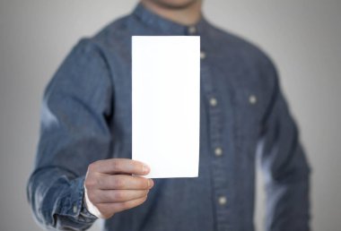 Bir adam beyaz bir kağıt parçası tutuyor. Bir adamın elinde bir el ilanı. Mesajın için hazır. Gri bir arkaplanda izole edilmiş.