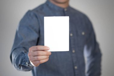 Bir adam beyaz bir kağıt parçası tutuyor. Bir adamın elinde bir el ilanı. Mesajın için hazır. Gri bir arkaplanda izole edilmiş.