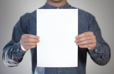 Bir adam beyaz bir kağıt parçası tutuyor. Bir adamın elinde bir el ilanı. Mesajın için hazır. Gri bir arkaplanda izole edilmiş.