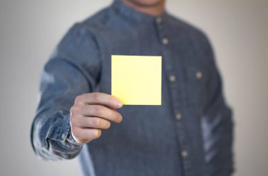 Bir adam sarı kare bir kağıt tutuyor. Bir adamın elinde bir el ilanı. Mesajın için hazır. Gri bir arkaplanda izole edilmiş.