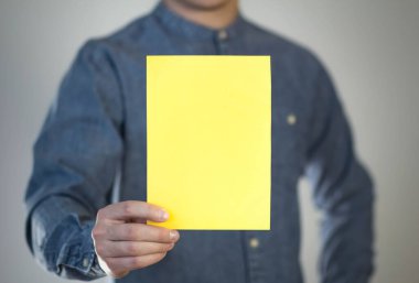 Bir adam sarı bir kağıt parçası tutuyor. Bir adamın elinde bir el ilanı. Mesajın için hazır. Gri bir arkaplanda izole edilmiş.