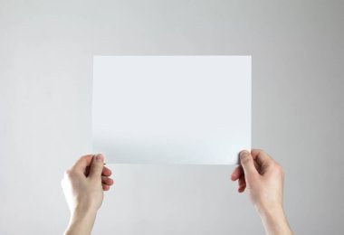 Ellerinde boş bir A4 kağıdı var. Elinde temiz bir el ilanı. Mesajın için. Gri bir arkaplanda izole edilmiş.