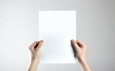Ellerinde boş bir A4 kağıdı var. Elinde temiz bir el ilanı. Mesajın için. Gri bir arkaplanda izole edilmiş.