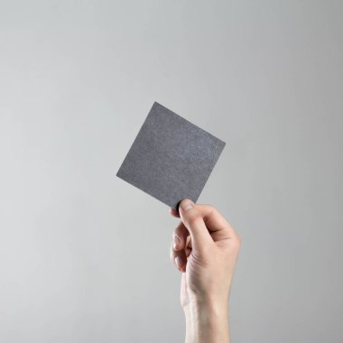 El boş bir kare siyah kağıt tutuyordu. Elinde temiz bir el ilanı. Mesajın için. Gri bir arkaplanda izole edilmiş.