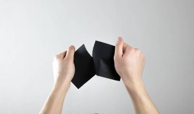 Eller siyah bir kağıt parçasını yırtıp atar. El ilanı. Gri bir arkaplanda izole edilmiş.