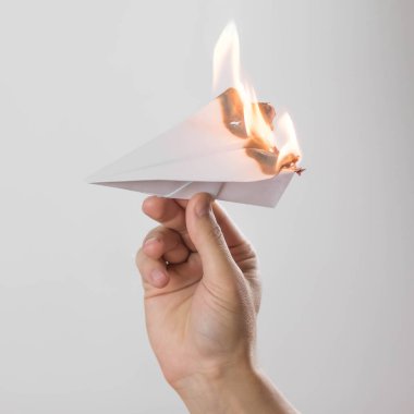 A hand holds a burning paper airplane. Close up. Isolated on a gray background.