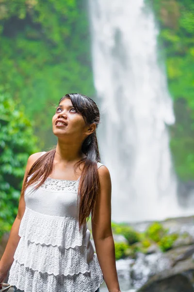 A young Asian woman at waterfall in rain forest gully looking at surroundings.