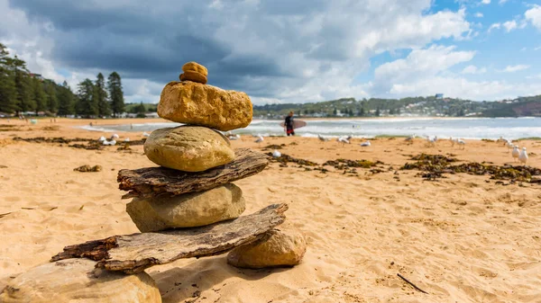 Batu Batu Ditumpuk Pantai Dengan Peselancar Berjalan Latar Belakang Yang Stok Gambar Bebas Royalti