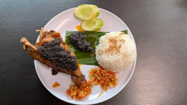 Özel siyah baharatlı Endonezya usulü kızarmış ördek (bumbu hitam), beyaz pirinç, mango acı biber sosu ve salatalık. Geleneksel Java yemekleri beyaz tabakta servis edilir..