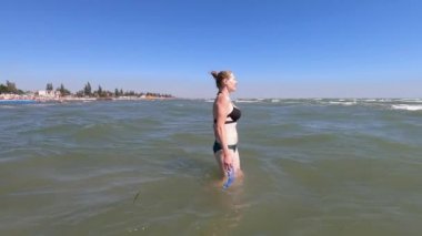 Güzel bir kadın yüzmek için okyanusa doğru yürür. Mavi gökyüzü. Yeşil mayo giymiş bir kadın..