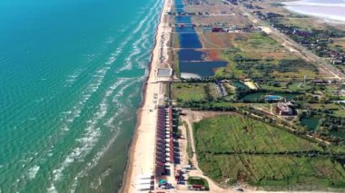 Yazın sahilde güzel bir uçuş. İnsanlar deniz kenarında dinleniyor. Turistler için evler. Plaj şemsiyeleri, gezintiler, denizde yüzen insanlar..