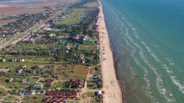 Yazın sahilde güzel bir uçuş. İnsanlar deniz kenarında dinleniyor. Turistler için evler. Plaj şemsiyeleri, gezintiler, denizde yüzen insanlar..