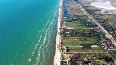 Yazın sahilde güzel bir uçuş. İnsanlar deniz kenarında dinleniyor. Turistler için evler. Plaj şemsiyeleri, gezintiler, denizde yüzen insanlar..