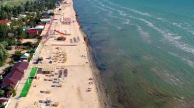 Yazın sahilde güzel bir uçuş. İnsanlar deniz kenarında dinleniyor. Turistler için evler. Plaj şemsiyeleri, gezintiler, denizde yüzen insanlar..