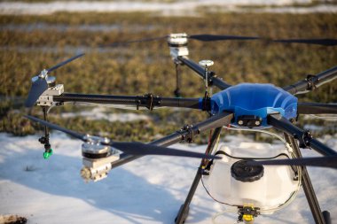 Sahada güzel mavi bir agrodron duruyor. Buğday yetişiyor. Kar henüz erimedi ki. Agrodronlar gübre püskürtmeye hazır..