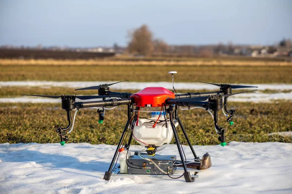 Sahada güzel bir kırmızı agrodron duruyor. Buğday yetişiyor. Kar henüz erimedi ki. Agrodronlar gübre püskürtmeye hazır..