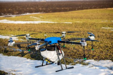 Sahada güzel mavi bir agrodron duruyor. Buğday yetişiyor. Kar henüz erimedi ki. Agrodronlar gübre püskürtmeye hazır..