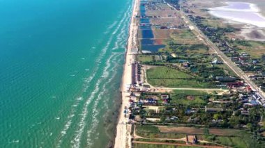 Yazın sahilde güzel bir uçuş. İnsanlar deniz kenarında dinleniyor. Turistler için evler. Plaj şemsiyeleri, gezintiler, denizde yüzen insanlar..
