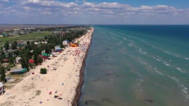 Yazın sahilde güzel bir uçuş. İnsanlar deniz kenarında dinleniyor. Turistler için evler. Plaj şemsiyeleri, gezintiler, denizde yüzen insanlar..