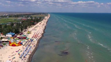 Yazın sahilde güzel bir uçuş. İnsanlar deniz kenarında dinleniyor. Turistler için evler. Plaj şemsiyeleri, gezintiler, denizde yüzen insanlar..